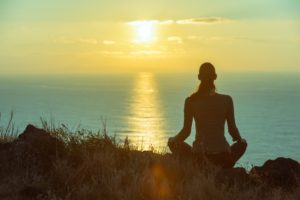 Woman meditating on cliff at sunset