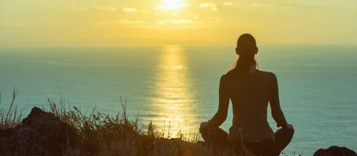Woman meditating on cliff at sunset